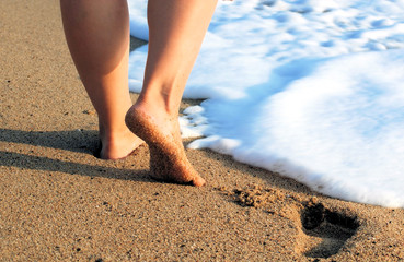 female feet on sea sand and white foam with a wave