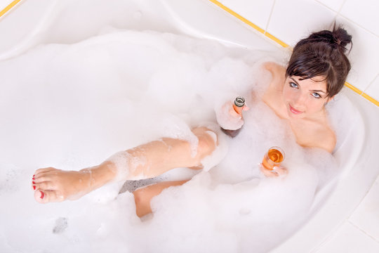 Young woman with champagne in the bathtub