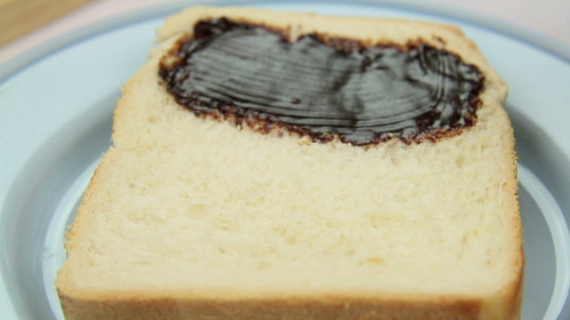 Vegemite being spread on to a slice of fresh bread.