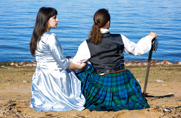 Fototapeta na wymiar Woman and man in scottish costume sitting near the sea