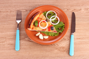 Pizza on plate and knife with fork on wooden table