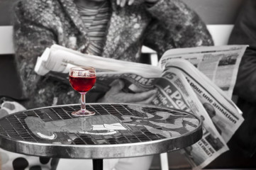 Obraz premium Lire le journal et boire un verre de vin rouge sur un table dans un bistrot parisien, couleur sélective - Paris France