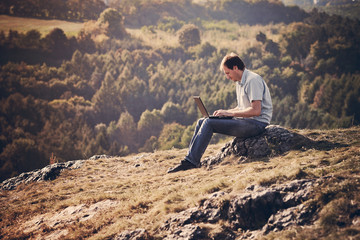 young man using laptop sitting on the grass on the hillside