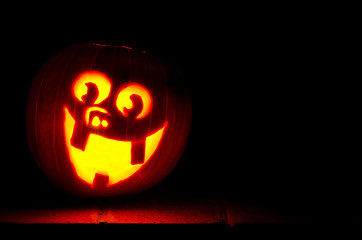 Carved happy jack-o-lantern on stoop at night.