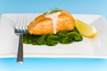 Salmon steak on spinach, decorated with lemon and sauce