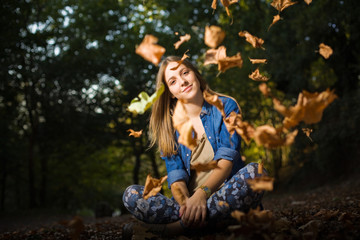 Beautiful young girl with falling leaves in the autumn park