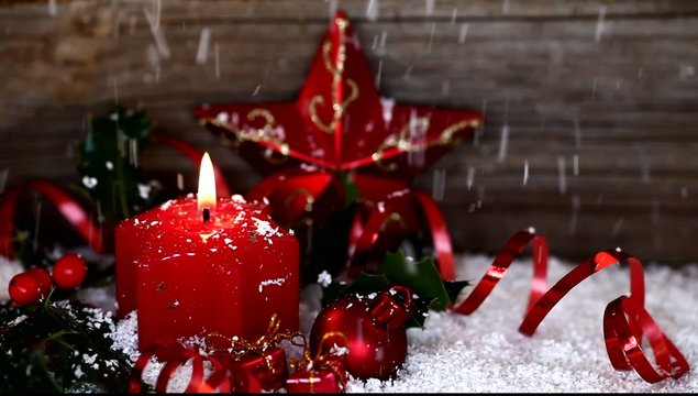 snow falling on red candle, holly and christmas decoration