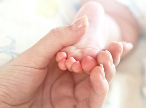 Mother hand holding new baby foot and doing massage