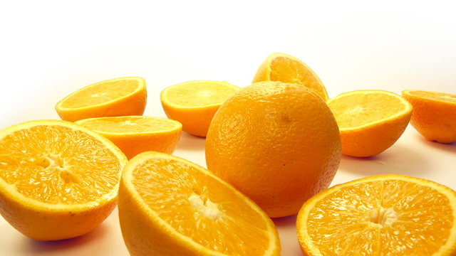 Close up of orange halves, one orange rolls to them.