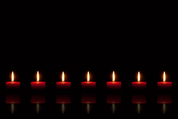 Sieben brennende rote Kerzen vor schwarzem Hintergrund