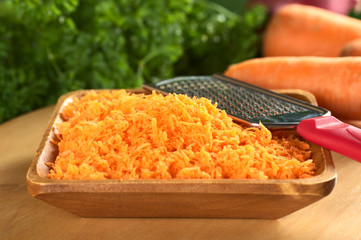 Fresh grated carrots in wooden bowl with grater