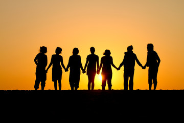 silhouette of group of friends standing in sunset at beach