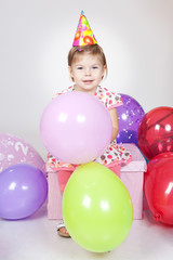 Obraz premium Little girl with balloons sitting on the gift in studio