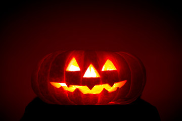 Fototapeta premium Orange scarry pumpkin with burning eyes, nose and mouth on dark