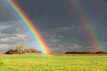Natural two rainbow over green field and dark sky