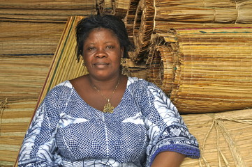 Afrikanische Frau sitzt vor Bastmatten