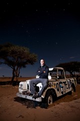 joyous man sits on broken stranded off-road vehicle hood, middle