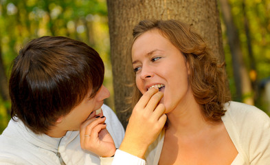 Loving couple feeding each other on candy in the park