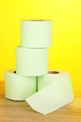 green rolls of toilet paper on wooden table on yellow background