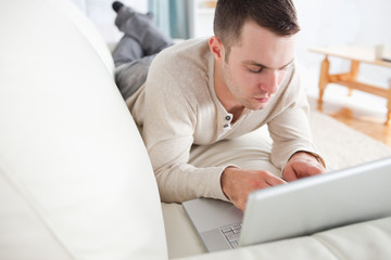 Good looking man lying on a couch using a laptop