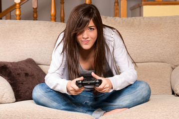 Obraz premium Young female playing video-games concentrating on sofa at home