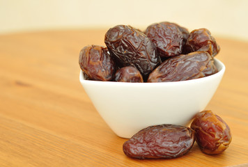 Medjool dates in a white bowl on wooden table.