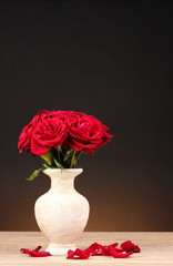 Fototapeta premium Beautiful red roses in vase on wooden table on brown background