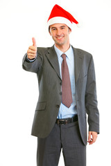 Smiling modern businessman in Santa Hat showing thumbs up