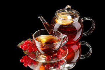 Glass teapot and cup with black viburnum tea isolated on black