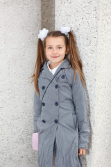 Little girl in grey coat standing near wall