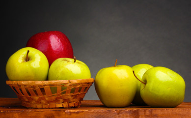 juicy sweet apples in basket on wooden table on gray background