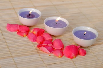 Obraz na płótnie Canvas three purple candles with rose petals on bamboo
