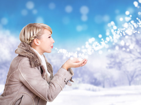 junge blonde Frau in Wintersachen pustet Schnee