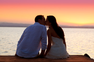 couple kissing at sunset sitting in jetty