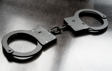 Black metallic handcuffs on wooden table