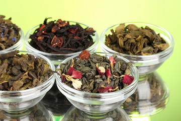 Different kinds of green and black dry tea on green background