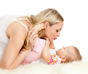 Obraz na płótnie Canvas Loving mother kisses her child; child is lying on sheepskin