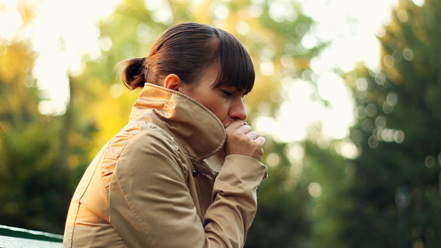 Sick woman sitting on park bench and coughing