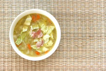Vegetable cabbage soup in white bowl with bacon pieces