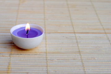 Obraz na płótnie Canvas lighted purple candle on bamboo place mat