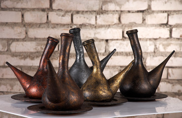 Different old metallic jugs in front of brick wall