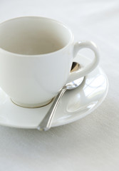 A white cup and saucer, empty, on a  table cloth