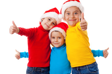Fototapeta premium Three smiling children in Santa hats with thumb up sign