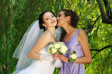 The young girl kisses the bride on a background of greens