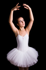 Teen girl ballet dancer standing in a tutu on a black background