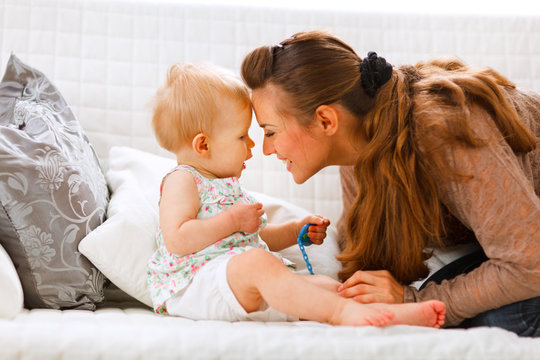 Cute baby with soother and young mom playing on divan