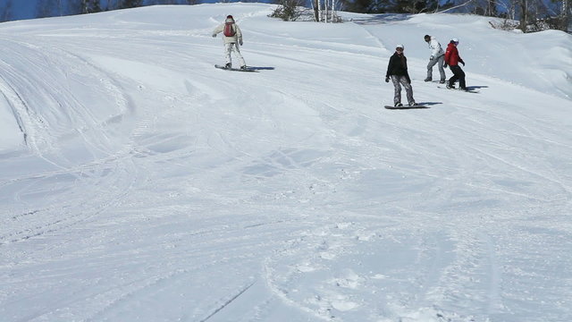 Four snowboarders taking a slow winding ride down the slope