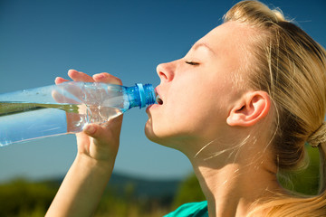 Young woman is drinking water outdoors