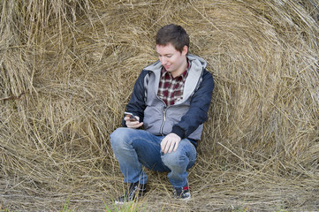 Naklejka na ściany i meble Man with phone sits near haystack