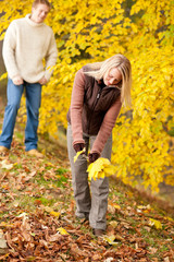 Autumn happy couple picking leaves in park